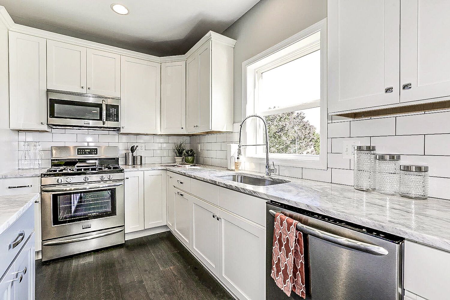 A kitchen with white cabinets , stainless steel appliances , granite counter tops and a window.