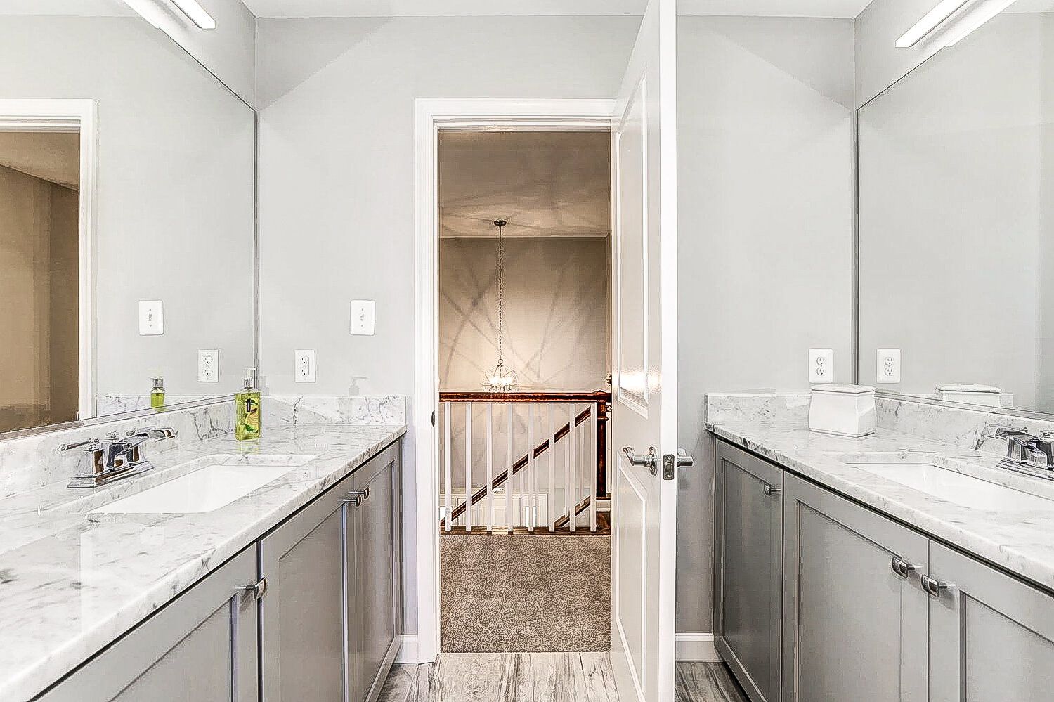 A bathroom with two sinks , two mirrors and a staircase.