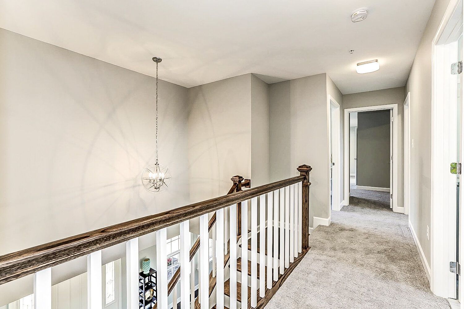 A hallway with a wooden railing and a chandelier hanging from the ceiling.