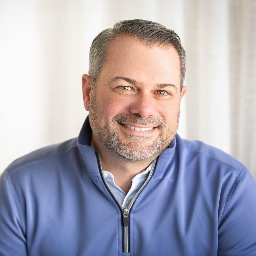 A man with a beard is wearing a blue sweater and smiling.