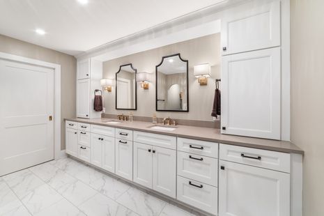 A bathroom with two sinks , two mirrors , and white cabinets.