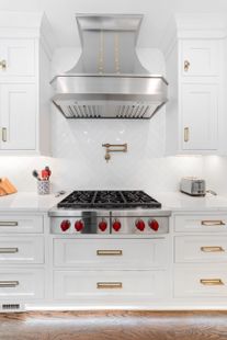 A kitchen with white cabinets and a stove top oven with red knobs.