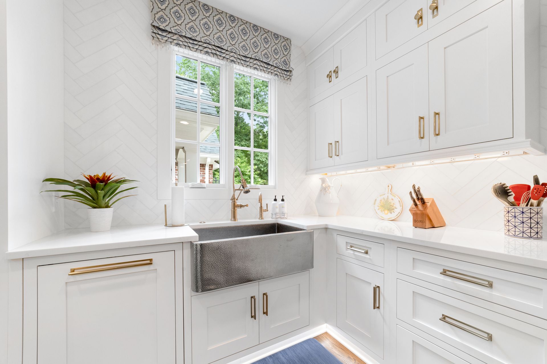 A kitchen with white cabinets , a sink , and a window.