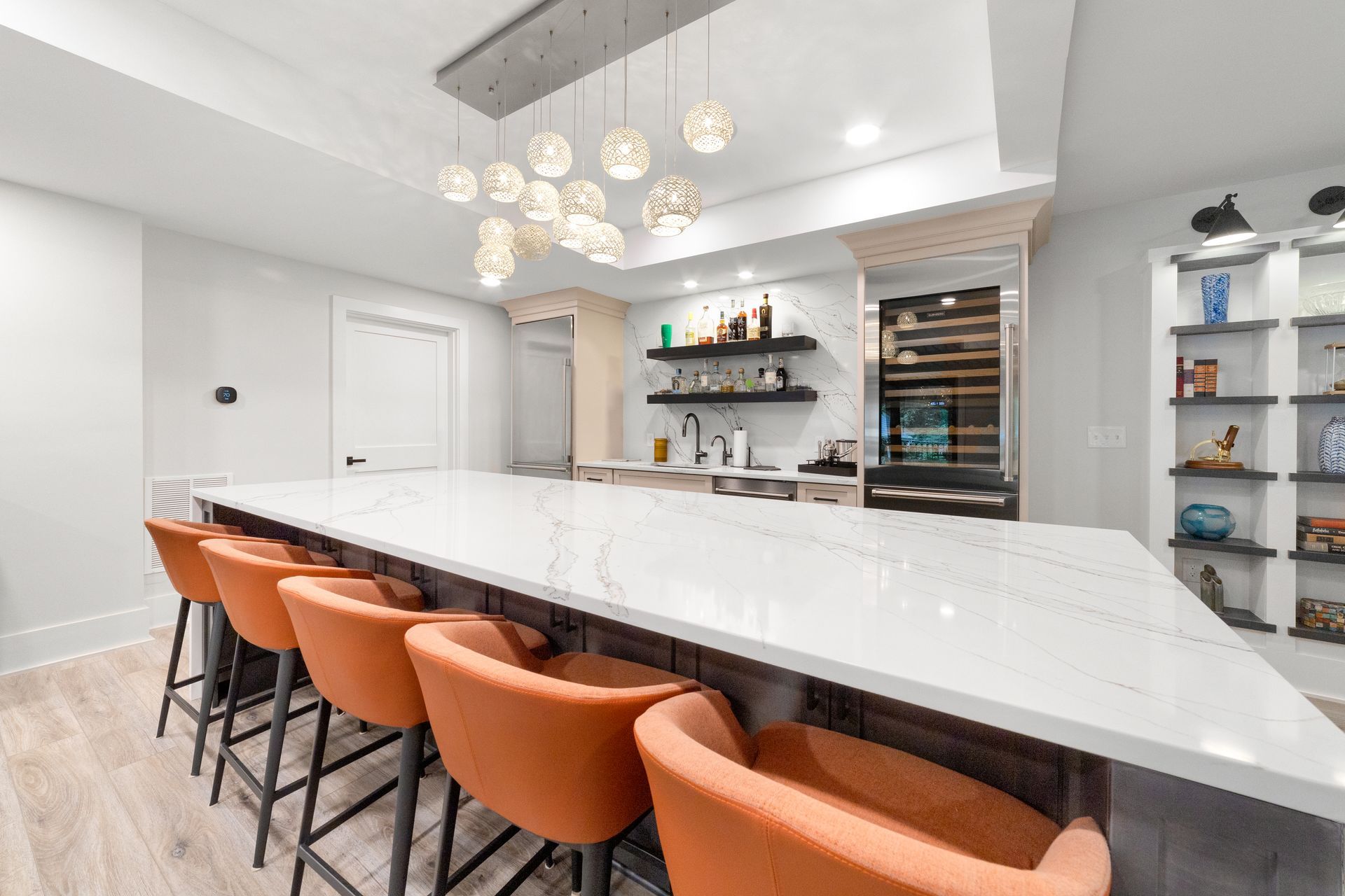 A kitchen with a long counter and orange chairs.