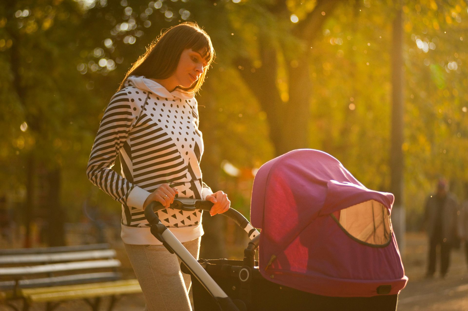 Woman pushing a stroller in a park bathed in sunlight.