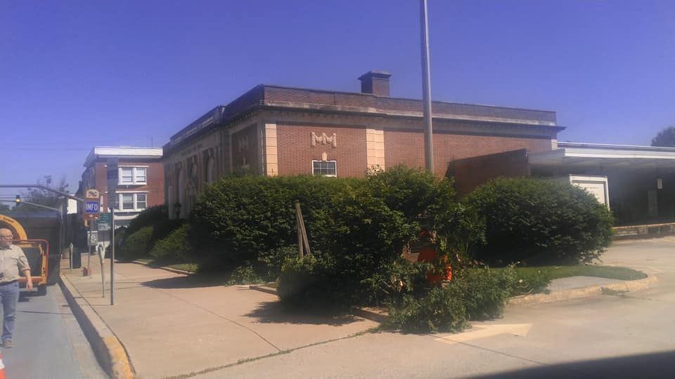 A large brick building is surrounded by bushes on a sunny day