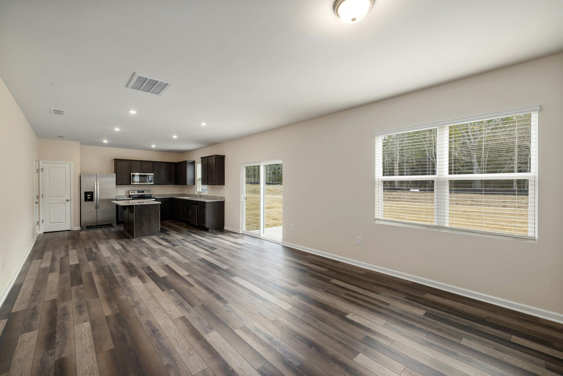 Open-concept living space with kitchen and dark wood-look floors. Includes a window and a door to the outside.