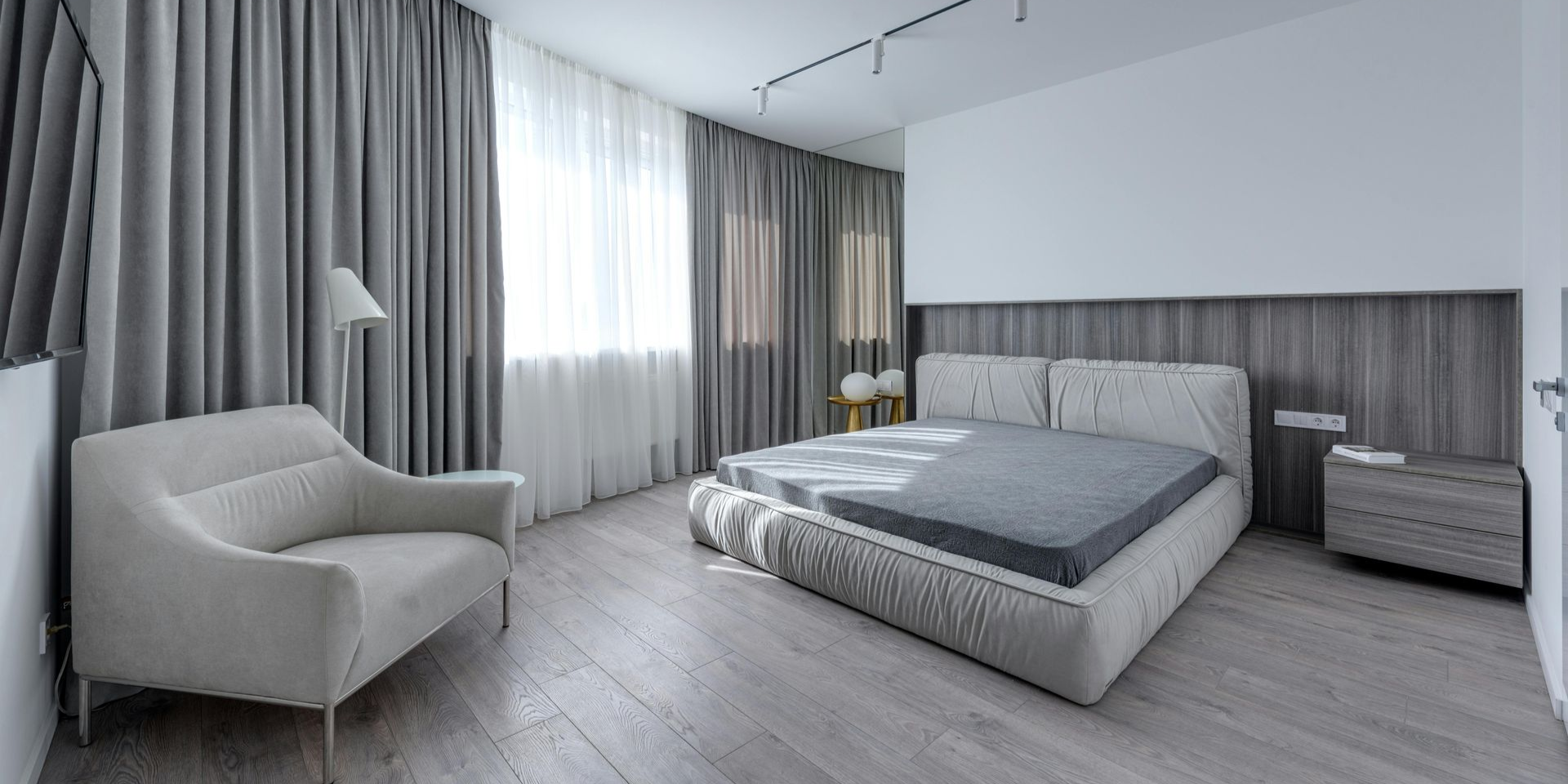 Bedroom with gray curtains, a bed, armchair, and nightstand.