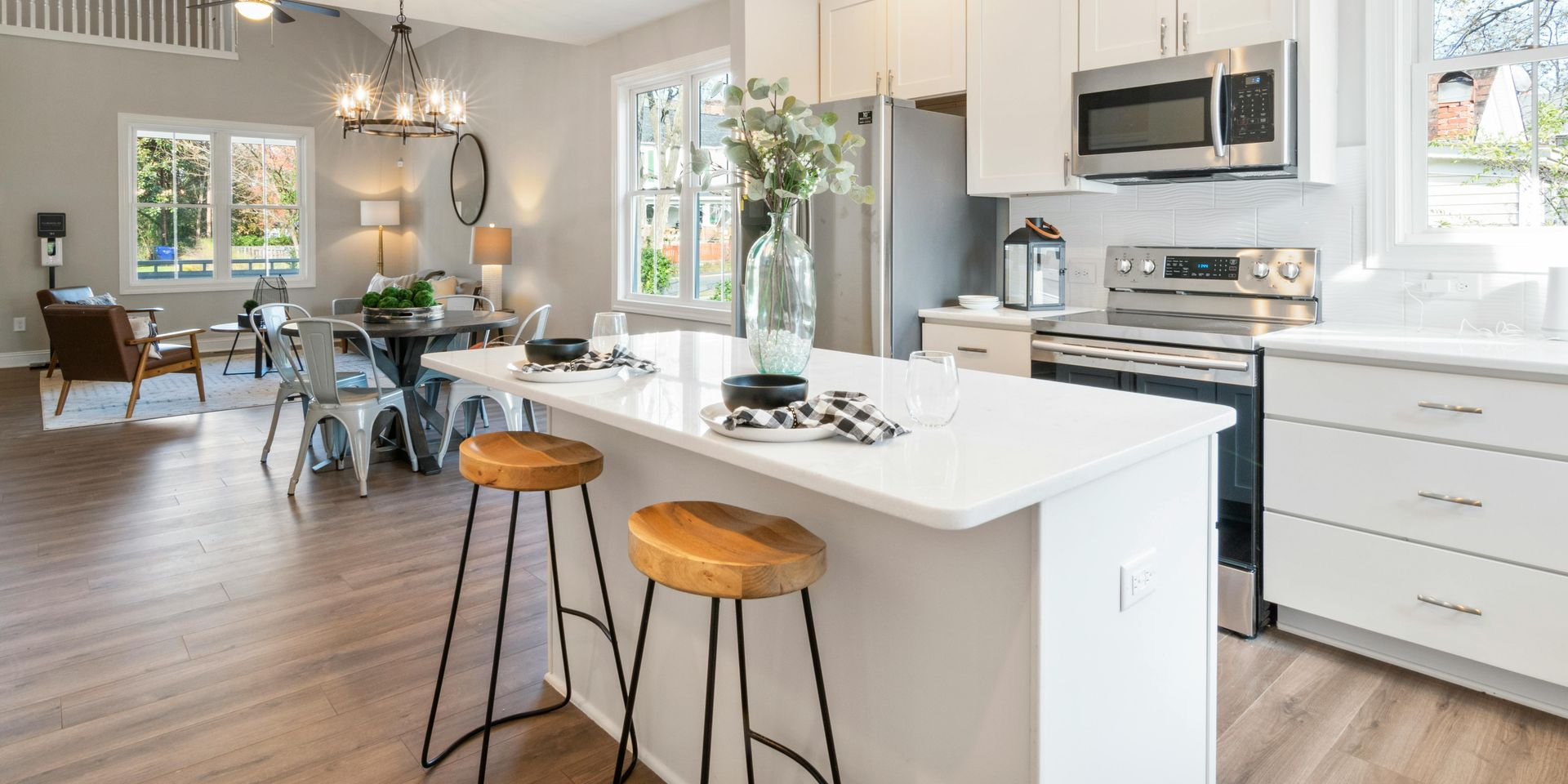 Modern kitchen with island, stools, and open dining area. White cabinets, stainless appliances, wooden floors.