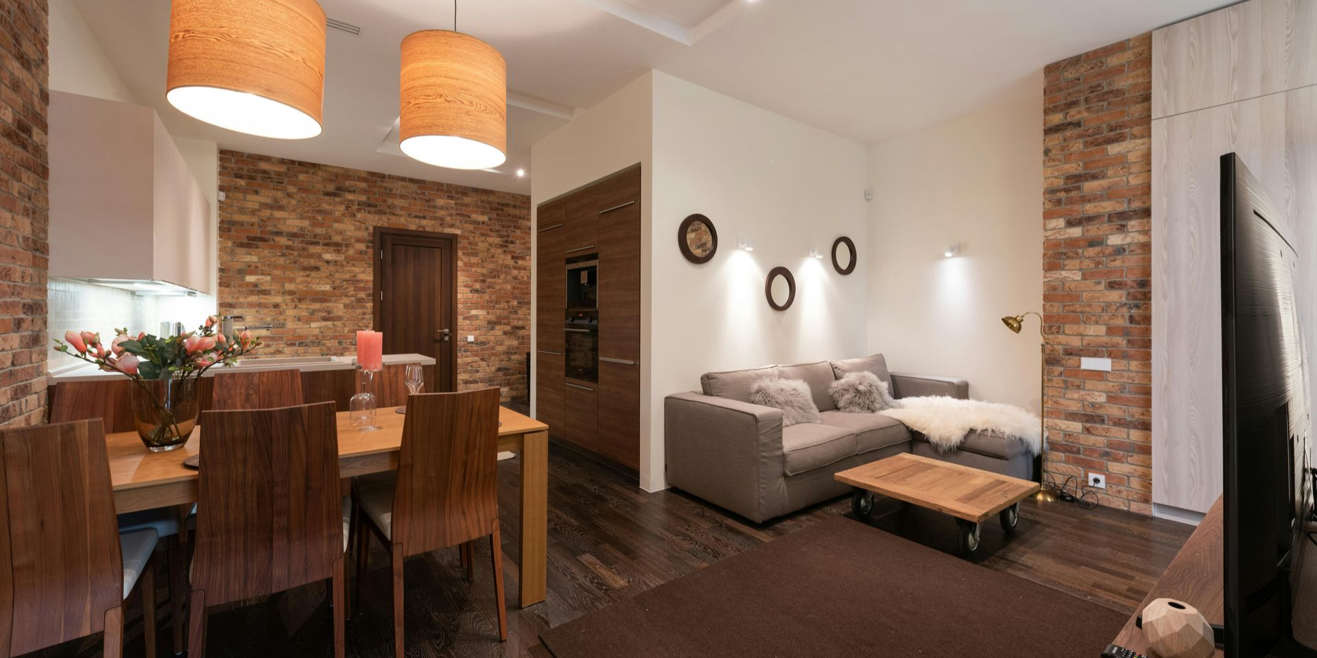A modern living room and dining area with brick walls, wood furnishings, and pendant lights.