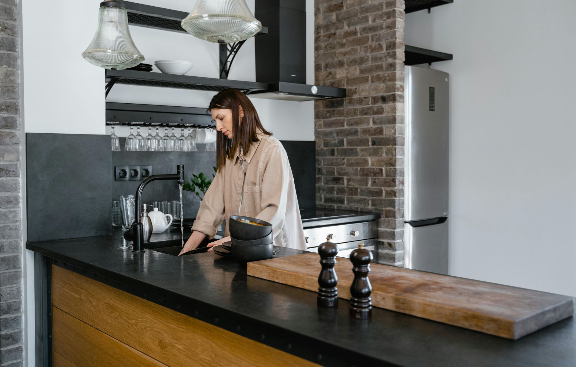 Woman standing at a kitchen sink, wooden countertop with bowls and salt/pepper shakers.