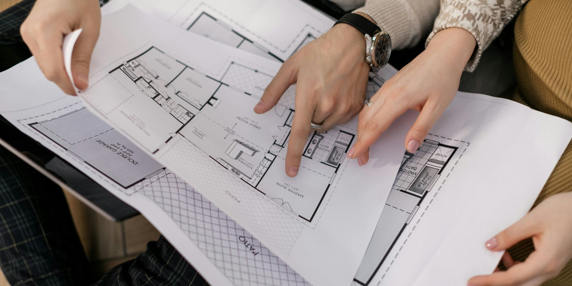 Two people reviewing blueprints, pointing at the layout, likely discussing a construction plan.