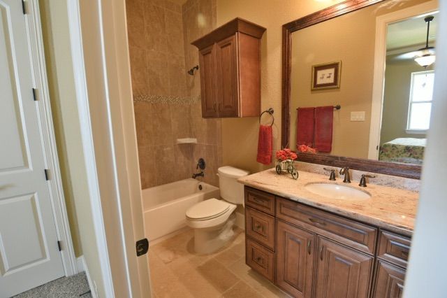 Bathroom with wooden vanity, toilet, tub, and tan tile walls.