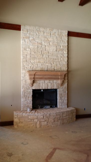 Stone fireplace with wooden mantel, set in a room with bare floors and neutral walls.