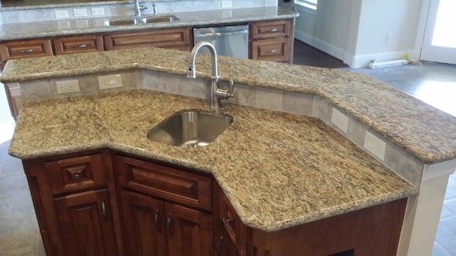 Kitchen island with granite countertop, sink, and brown cabinets.