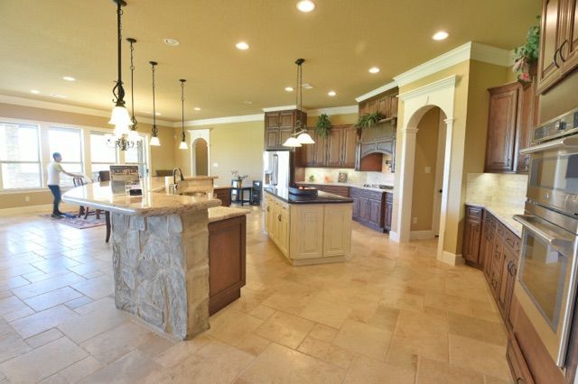 Spacious kitchen with multiple islands, stone countertops, and brown cabinets, open to a dining area.