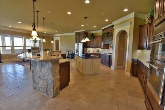 Spacious kitchen with stone island, wooden cabinets, and beige tile floor.