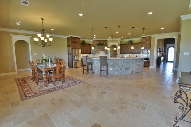 Spacious kitchen and dining area with stone island, wooden cabinets, and large chandelier.