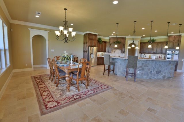 Open-concept kitchen and dining room with table, chairs, rug, and pendant lights. Tan walls, stone island, and wood cabinets.