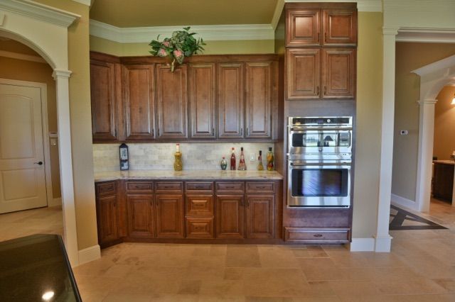 Kitchen cabinetry with built-in oven and countertop. Wooden cabinets, beige walls and floors.
