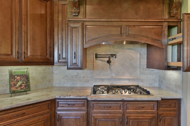 Brown kitchen cabinets with range hood and tiled backsplash.