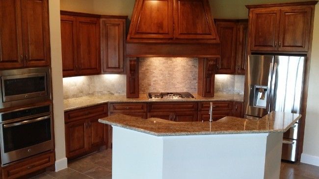 Kitchen with cherry-stained cabinets, granite countertops, stainless steel appliances, and a light-colored island.