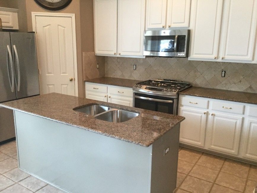 Kitchen with white cabinets, brown countertops, and a gray island with a sink.