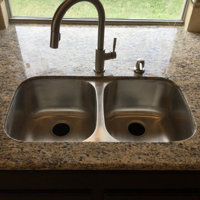 Stainless steel double sink with faucet and soap dispenser on speckled granite countertop.