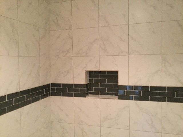 White tiled shower with a dark gray brick-like accent band and built-in niche.