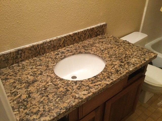 Bathroom vanity with oval sink, granite countertop, and dark wood cabinet. The walls are beige.