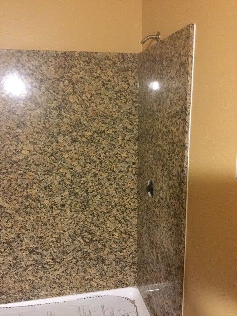 Granite-look shower wall with a faucet and the edge of a bathtub. Tan and brown colors.