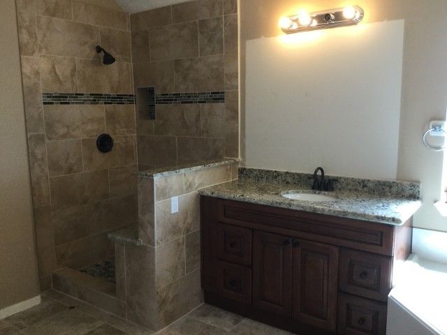 Bathroom with tile shower, vanity with dark wood cabinet, and granite countertop. Beige and brown tones.