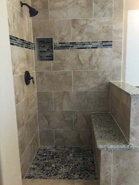Tiled shower with pebble floor, built-in bench, dark bronze fixtures, and a decorative tile band.