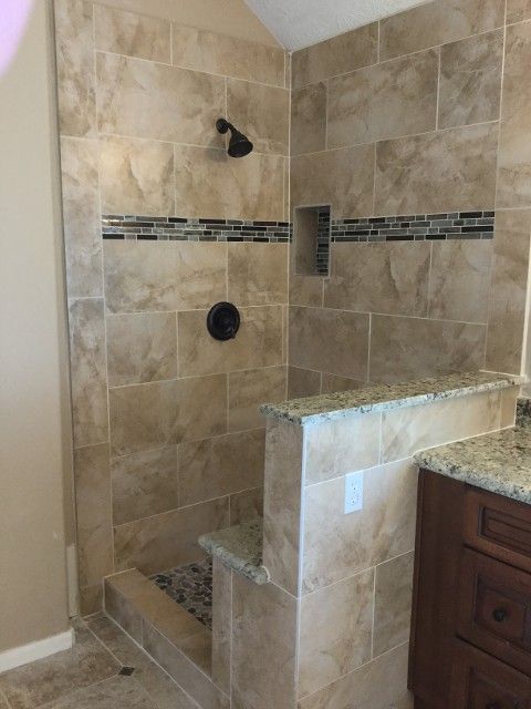 Tiled shower with dark fixtures and a low wall, beige and brown tones.