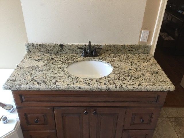 Bathroom vanity with granite countertop and oval sink. Brown wooden cabinet with dark faucet.