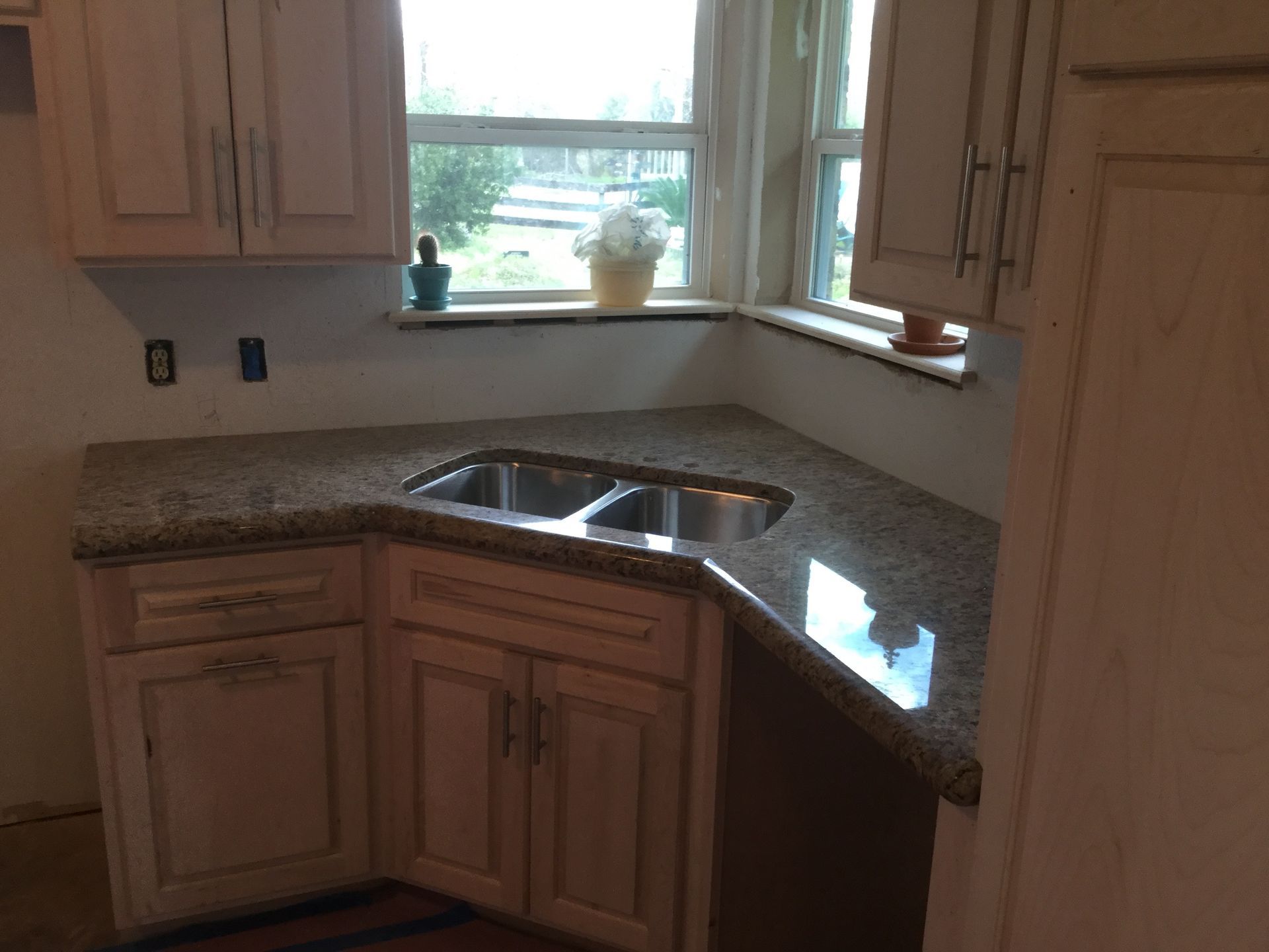 Corner kitchen sink with granite countertop and cabinets under a window.