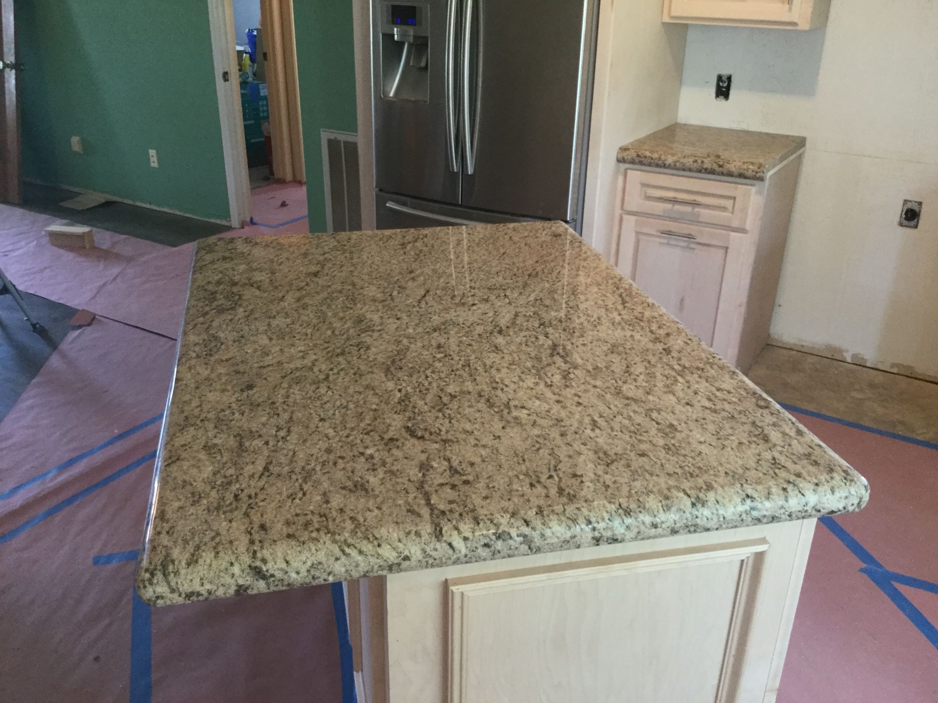 Granite countertop on a kitchen island, beige cabinets, partially constructed kitchen.