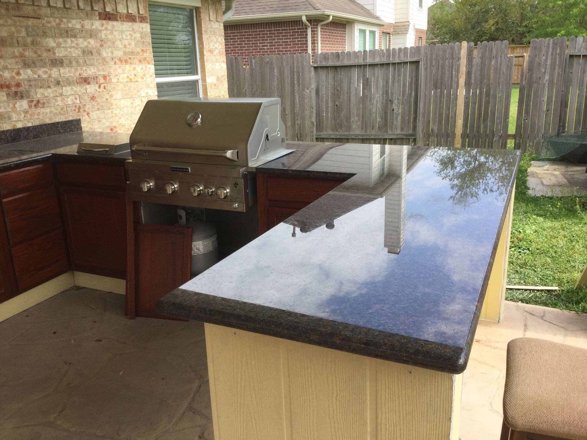 Outdoor kitchen with built-in grill, granite countertops, and dark cabinets.