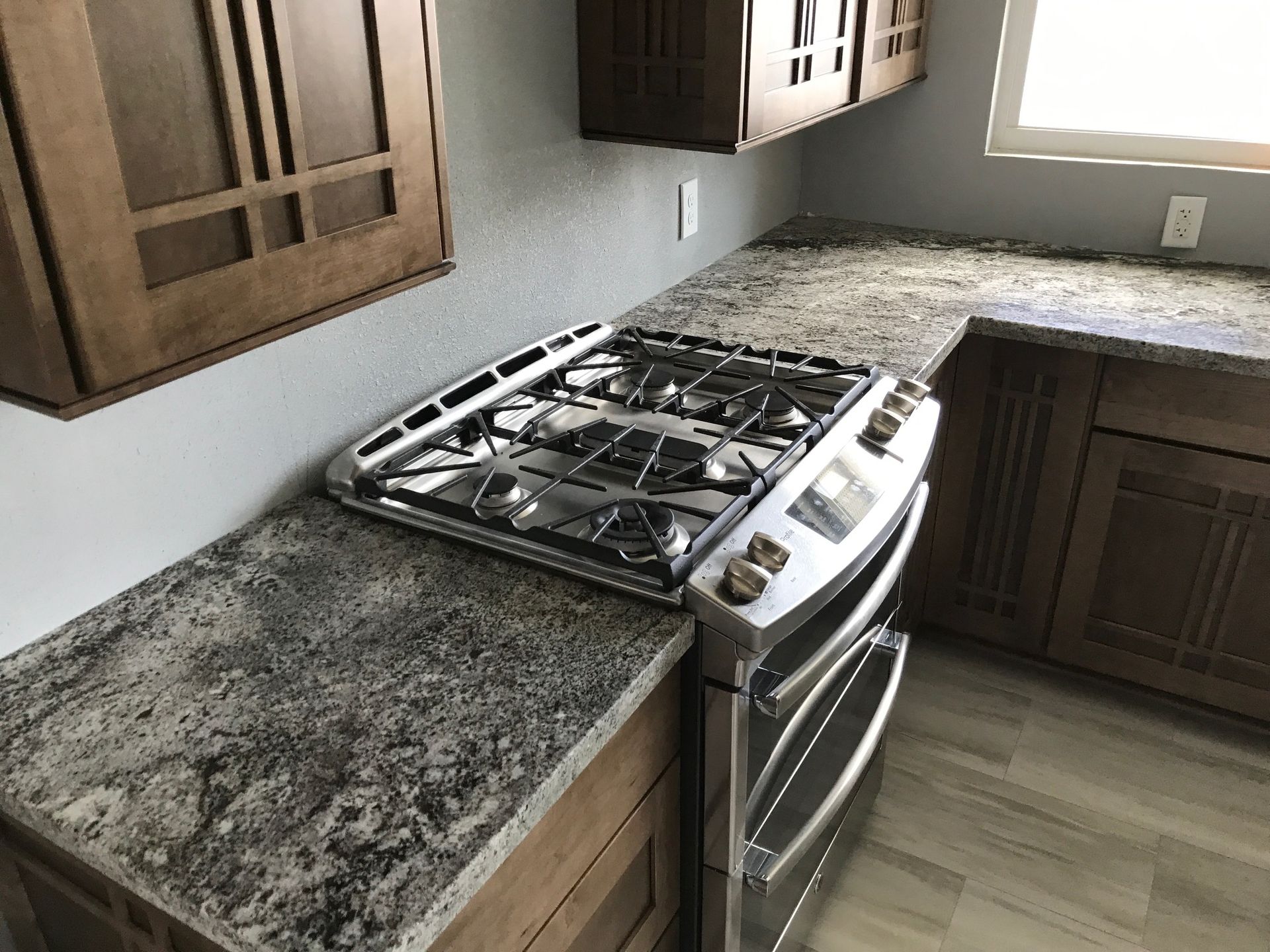 Kitchen with brown cabinets, gray countertop, and stainless steel gas range.