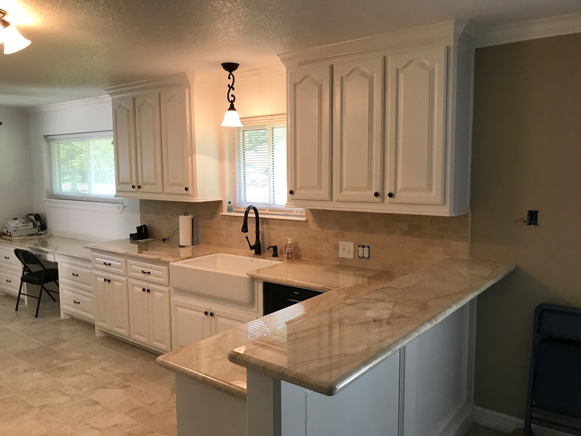 White kitchen with marble countertops, cabinets, and a farmhouse sink.