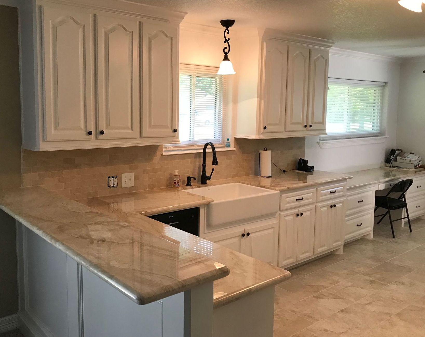 Bright white kitchen with beige countertops, cabinets, sink, window, and a small table by the wall.