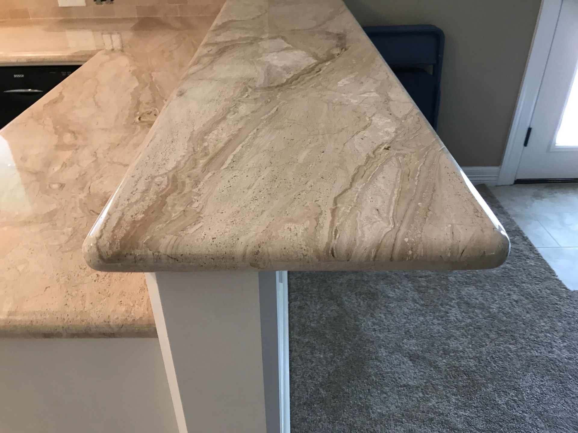 Beige stone countertop with rounded edges, supported by a white cabinet.