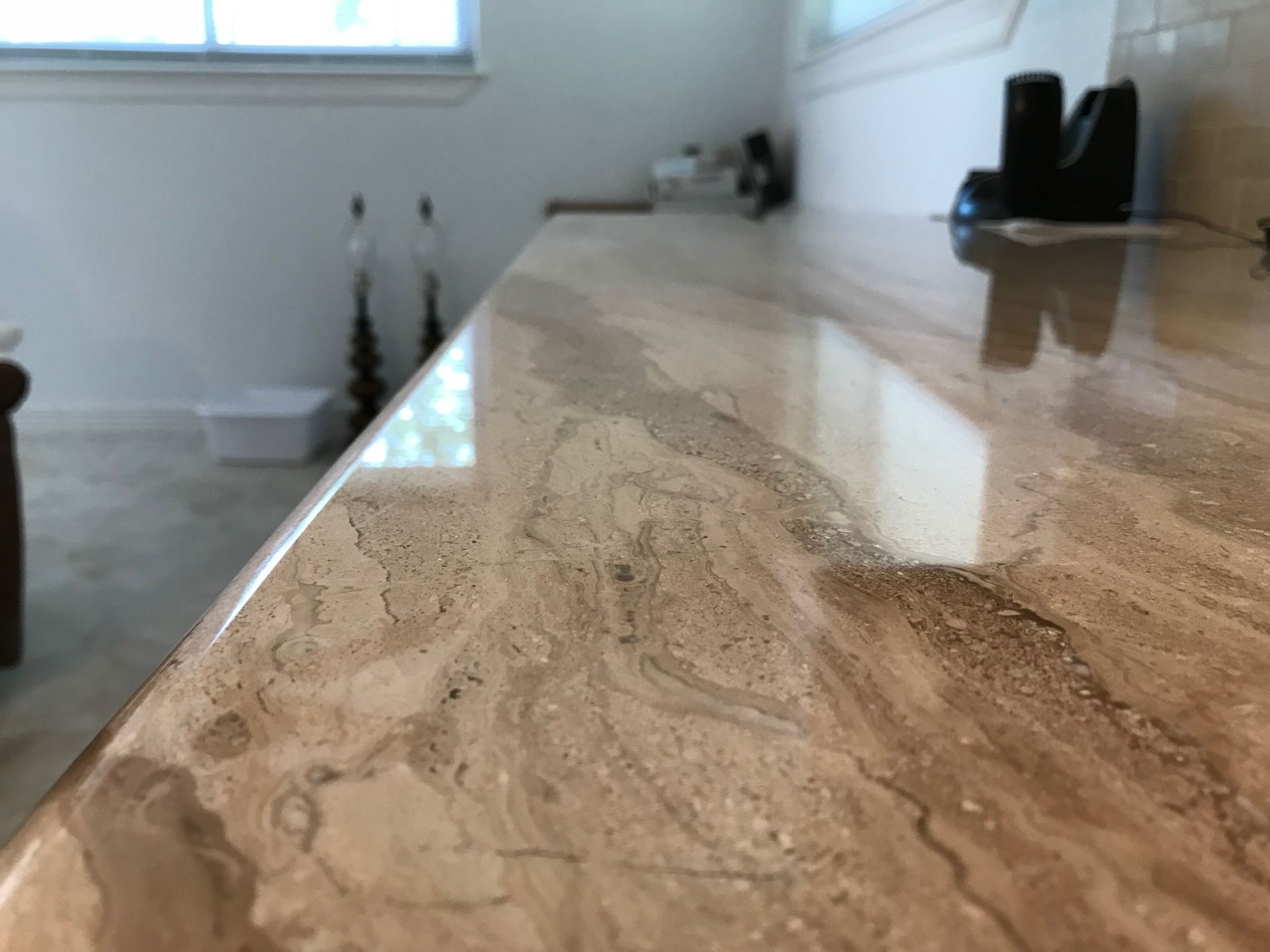 Close-up of a polished countertop with brown and tan veining. A white room and window are in the background.