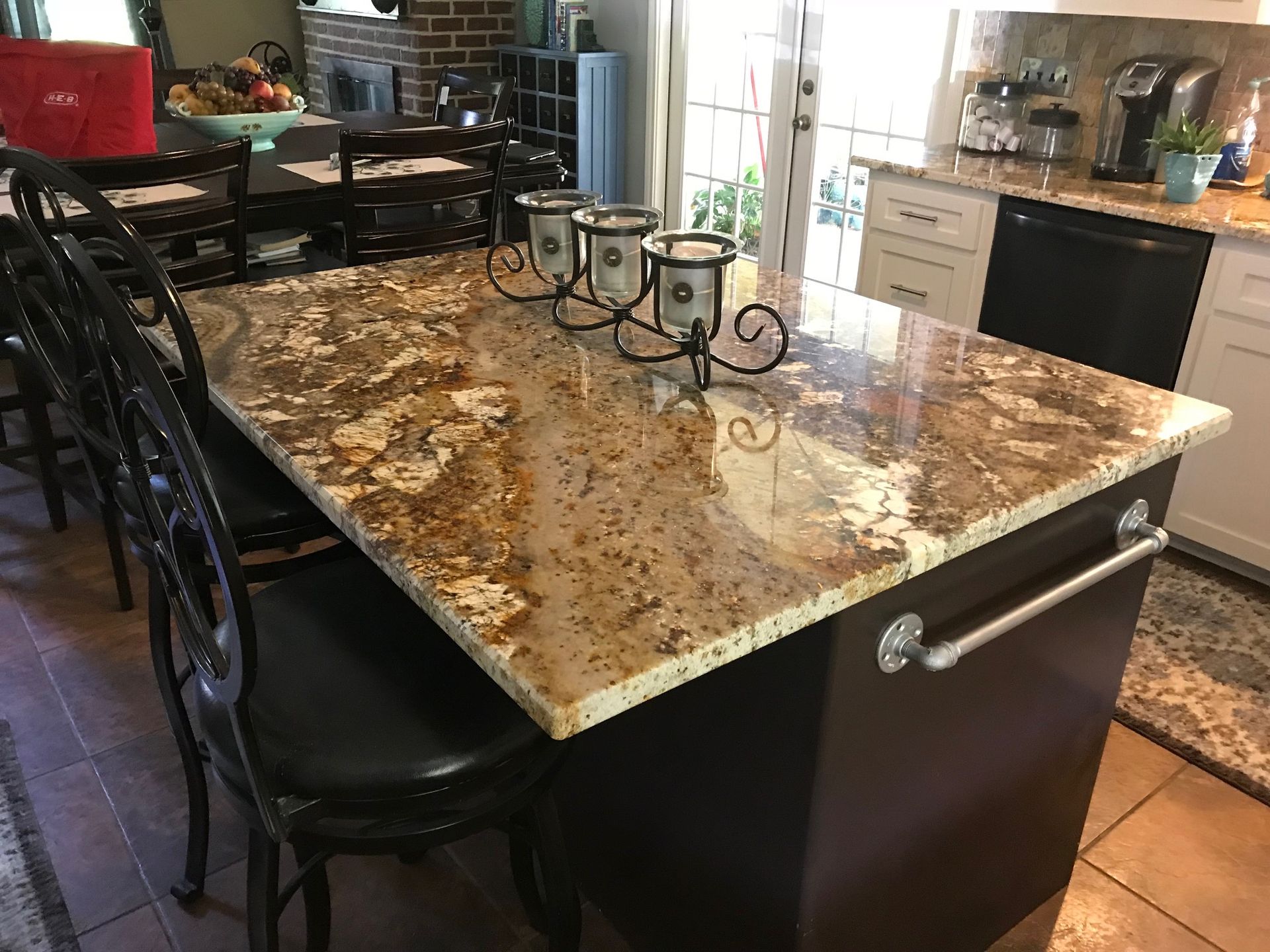 Kitchen island with granite countertop and seating. Dark cabinetry, ornate black chairs, and a candleholder.