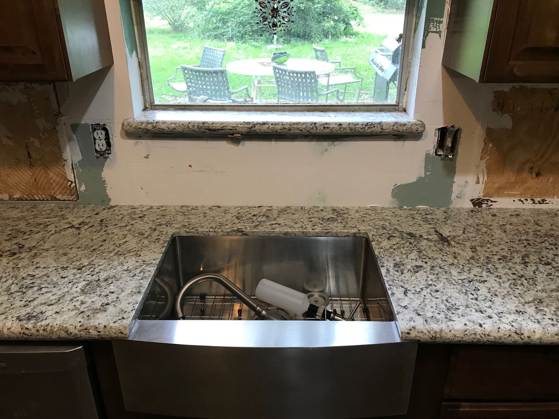 Kitchen sink installed in granite countertop, backsplash incomplete, window in background.