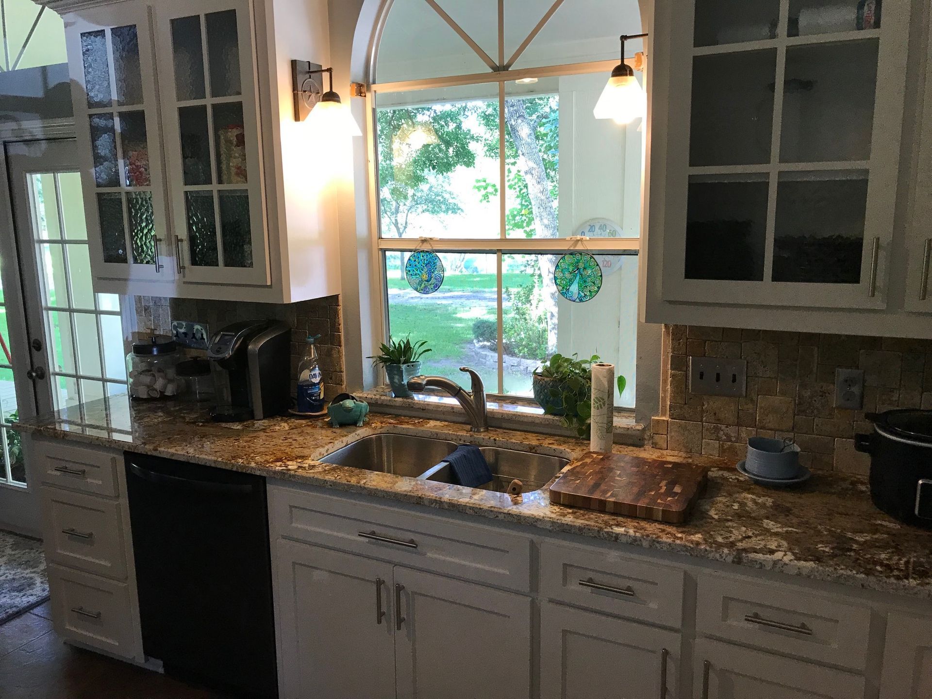 Kitchen with white cabinets, granite countertops, and a window over a sink. A dishwasher is to the left.