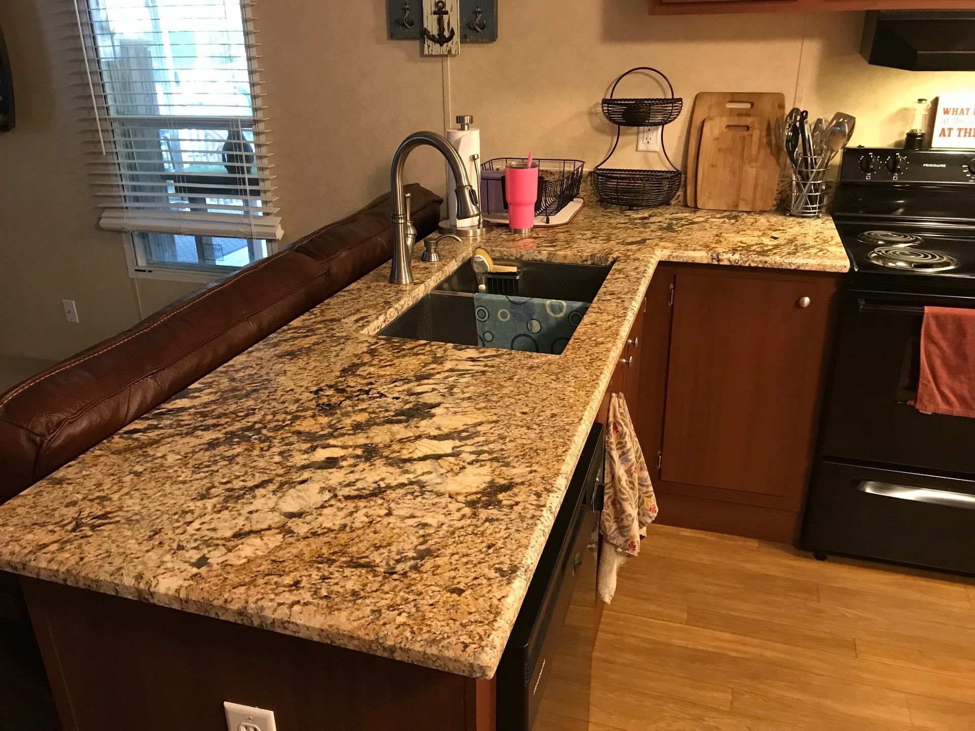 Kitchen with granite countertop, sink, and stove. Brown cabinets, tan walls, and a window.