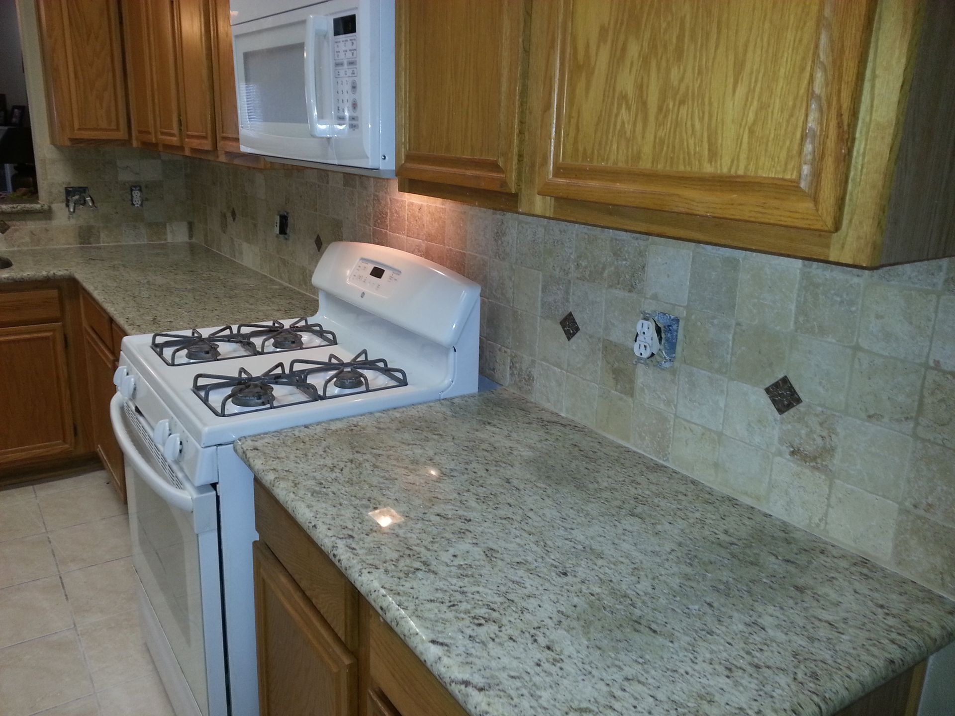 Kitchen with granite countertops, light brown cabinets, white stove, beige backsplash tiles.