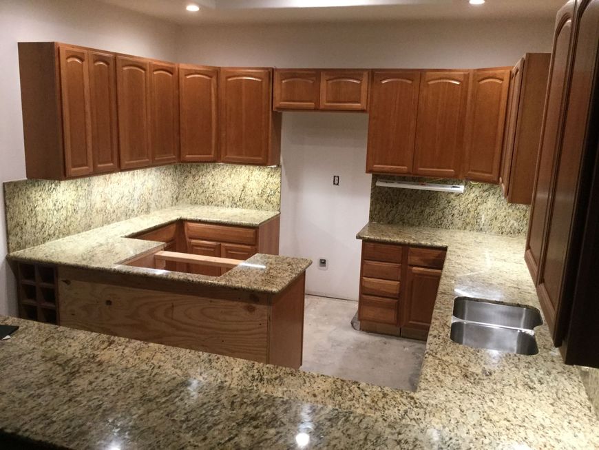 Empty kitchen with wood cabinets, granite countertops, and a central island under warm lighting