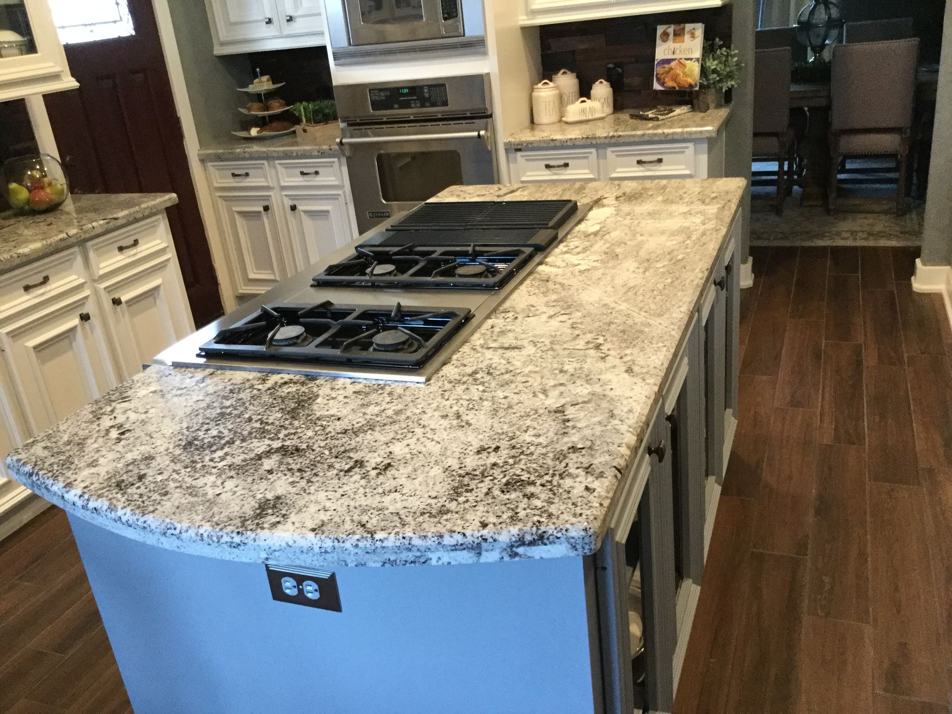 Kitchen island with granite countertop and cooktop; white cabinets and dark wood floor.
